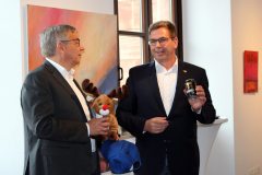 (FOTO: Inken Paletta/DFG Hessen e.V.) Oberbürgermeister Gert-Uwe Mende freut sich über die Finnland-Überraschung (Ein blaues Finnland-Käppi, ein Plüschrentier und ein finnisches Karhu-Bier. Der Bär ist in Finnland u.a. ein Symbol für Stärke.